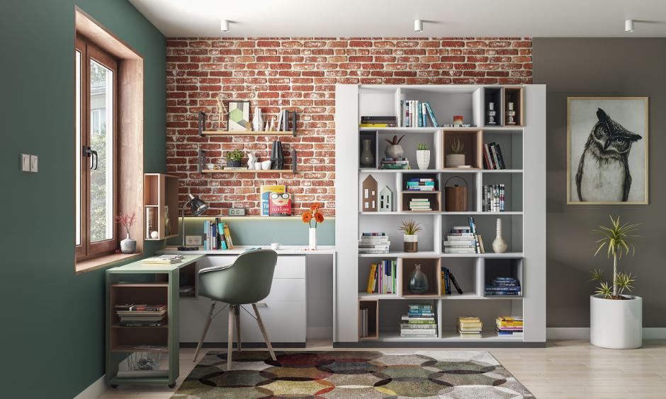 Small home office with a window-side movable desk, vertical bookshelves, floating shelves, and natural light.