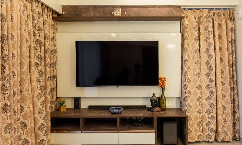 A minimalist TV unit with glossy cream and matte brown finish in a 2bhk interior